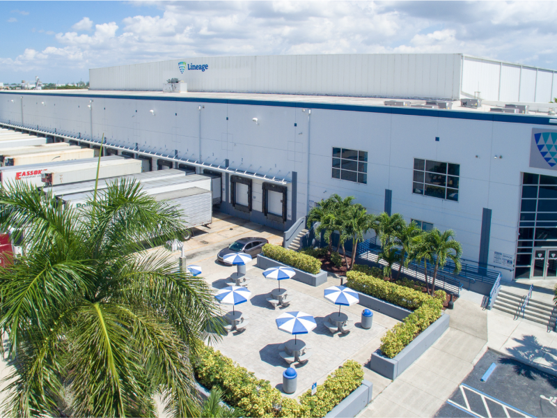 Aerial view of Lineage Logistics cold storage facility in Miami showcasing the expansive warehouse, loading docks with trucks, and the landscaped outdoor area with shaded seating.