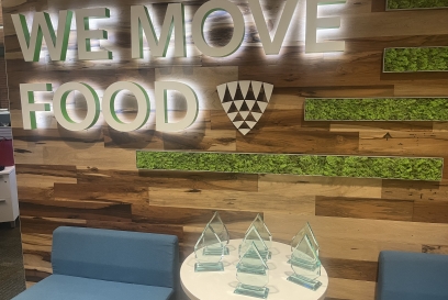 A group of trophies sit on a table in front of a wall decorated with the words We Move Food