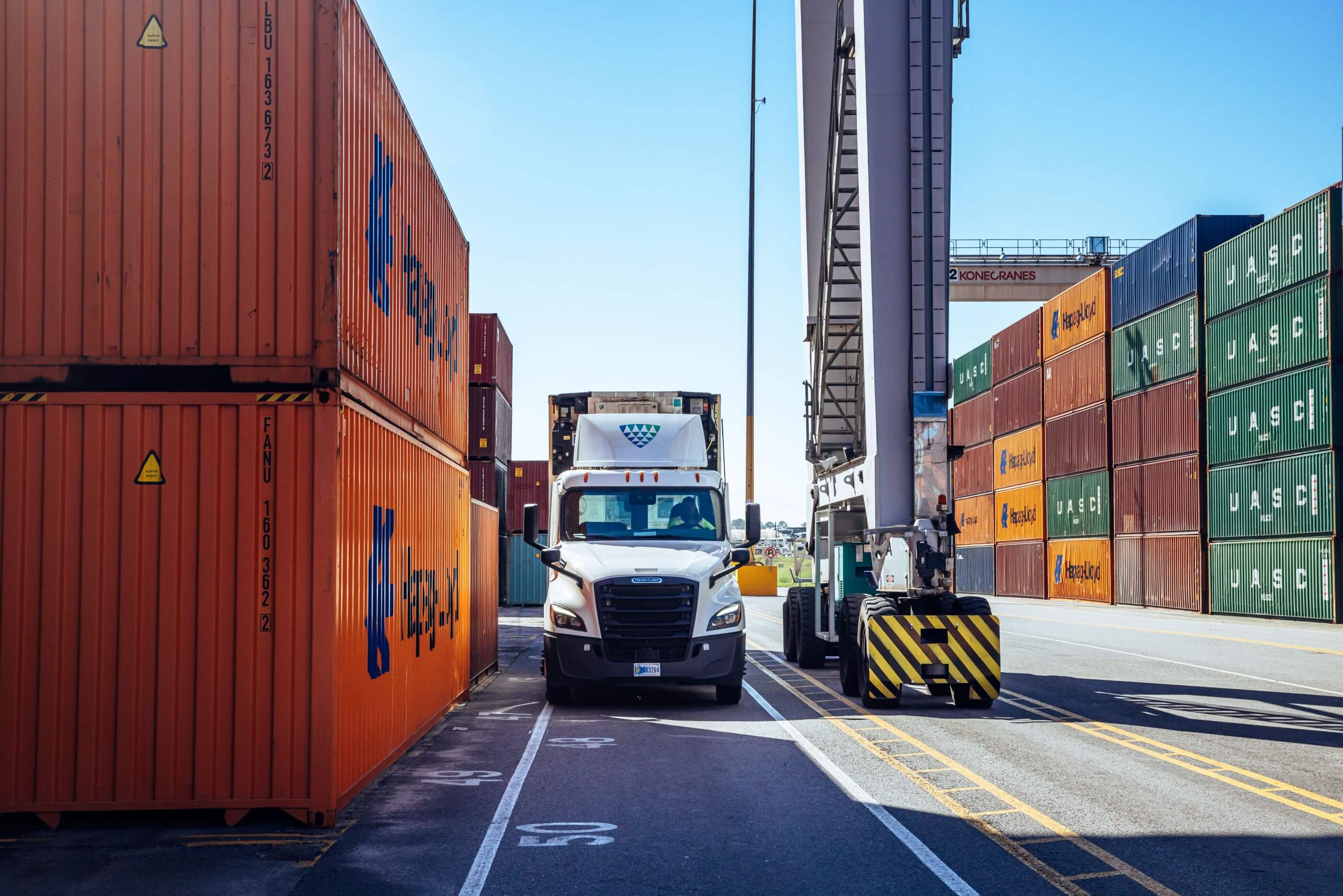 A Lineage semi-truck navigating between stacks of colorful shipping containers at a port.