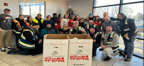 A group of Lineage team members gathered inside, smiling around two large donation boxes for the Toys for Tots program.